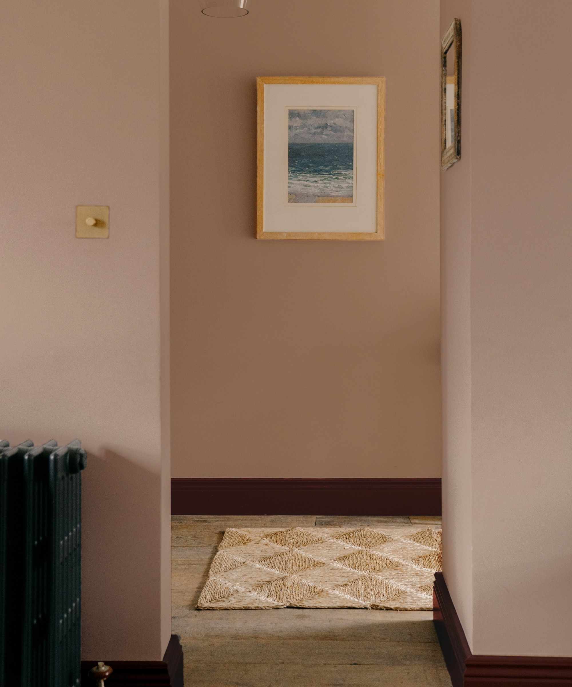 A pink hallway painted in COAT's Sybil with contrasting dark red skirting boards in Smith & The Devil