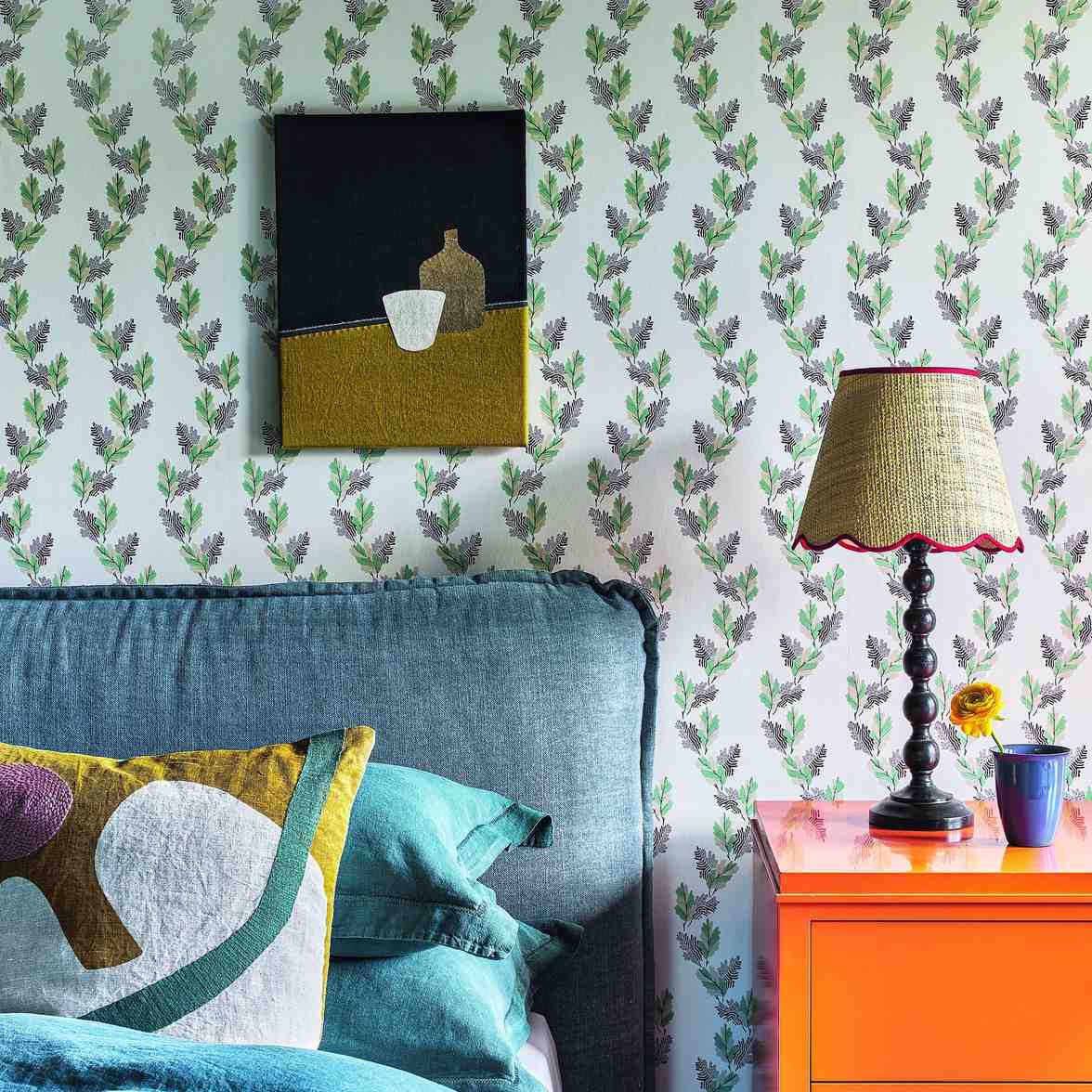 Bedroom with floral wallpaper, bed, orange bedside table and bobbin lamp.