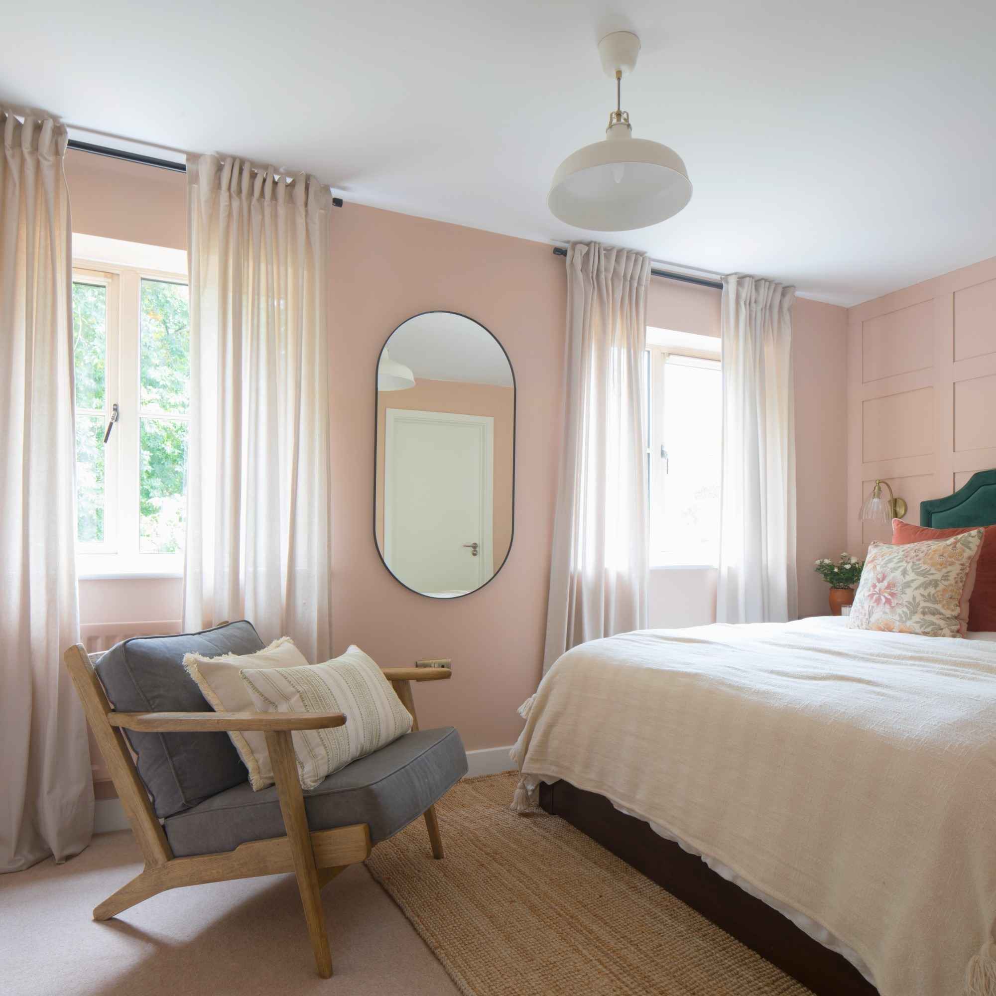 A pink-painted bedroom with a panelled wall behind the bed and an oval mirror hung on another wall