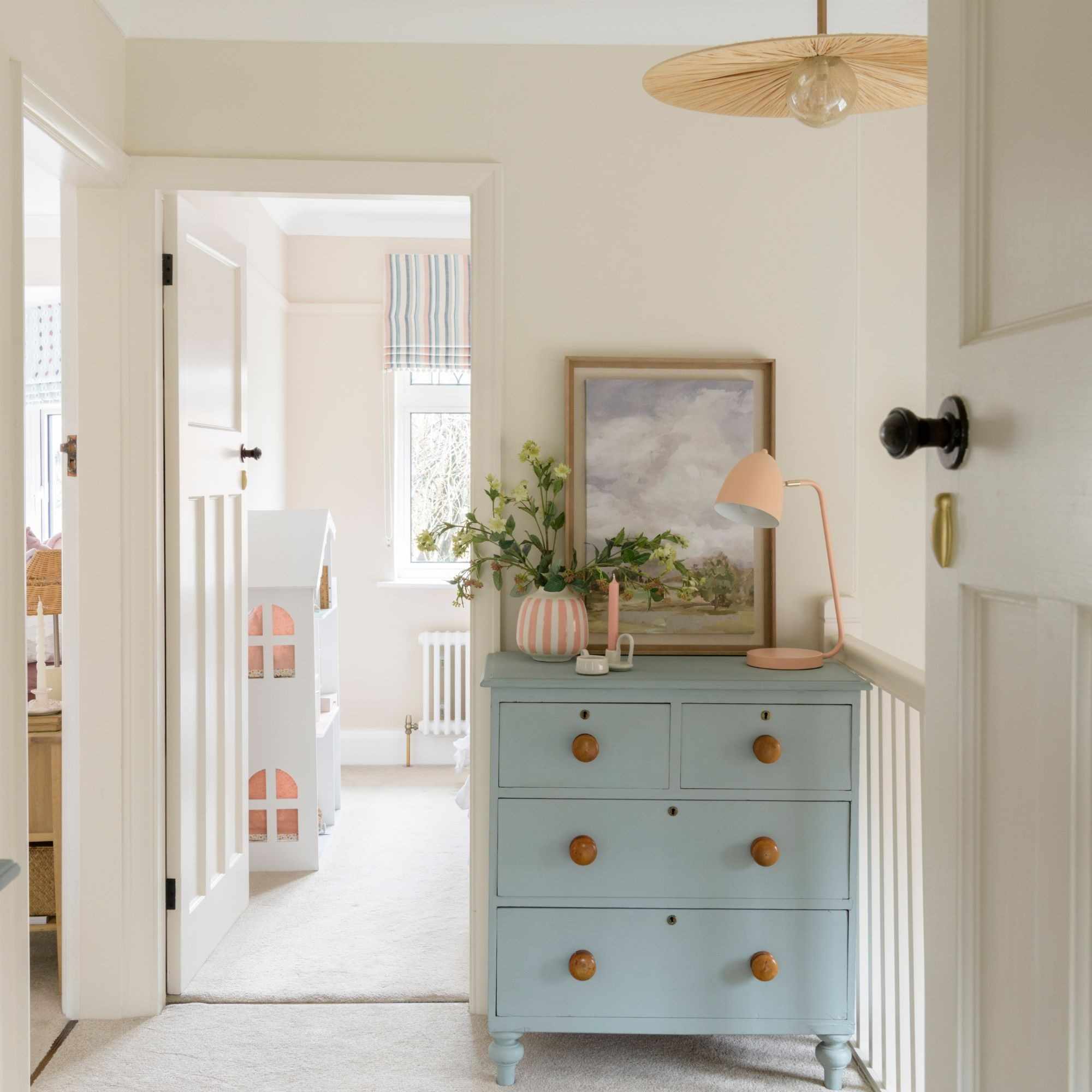 Cream coloured landing area with blue painted chest of drawers with trinkets on it, looking into a nursery room
