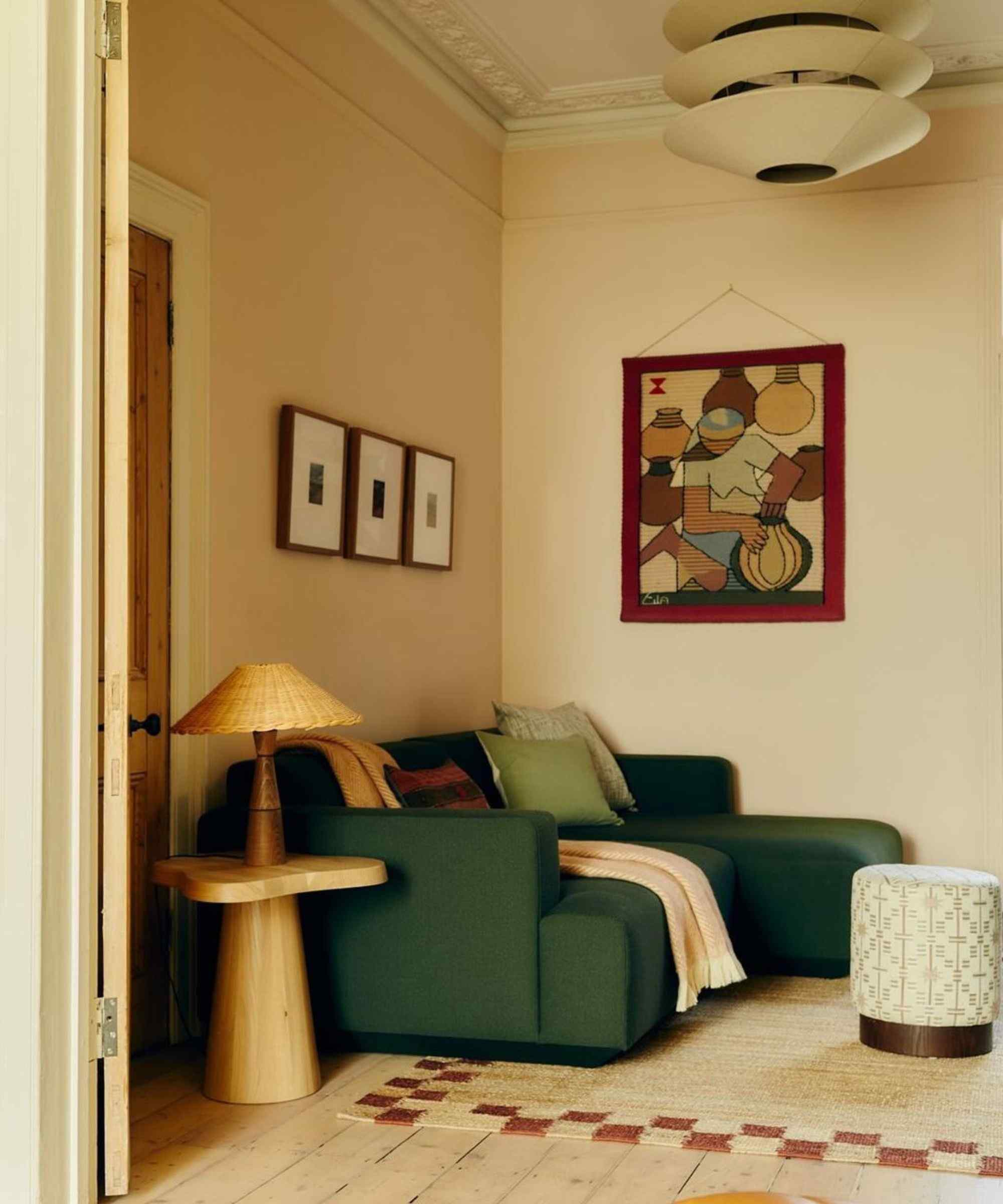 Living room with pale pink walls, green sofa, wood floor boards, jute rug, wood side table and rattan lamp