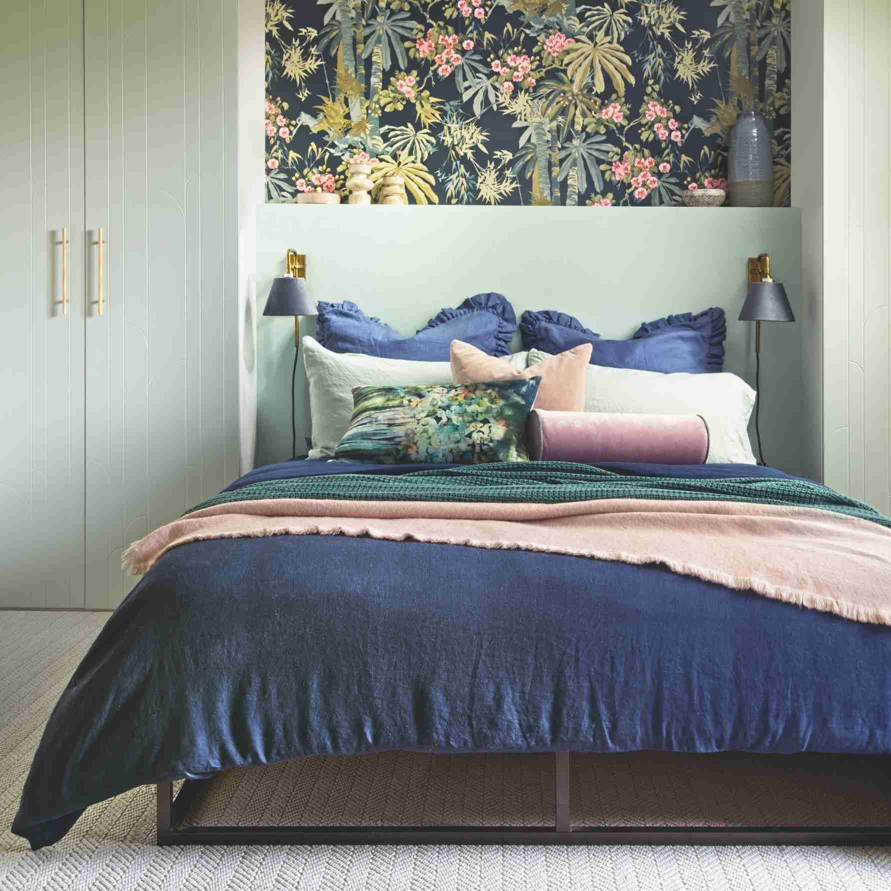 Green painted bedroom with blue and pink bedding and fitted wardrobes either side of the bed