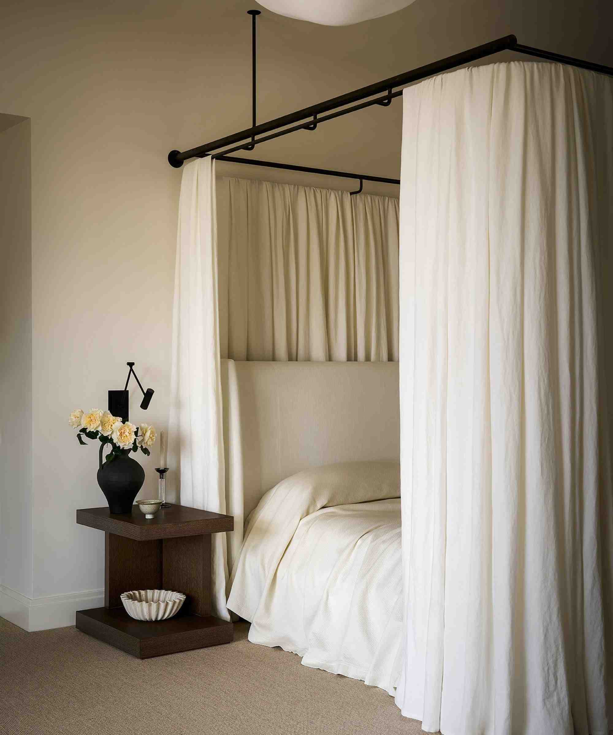 neutral minimalist bedroom with a canopy bed and white bedding, and a dark wooden nightstand