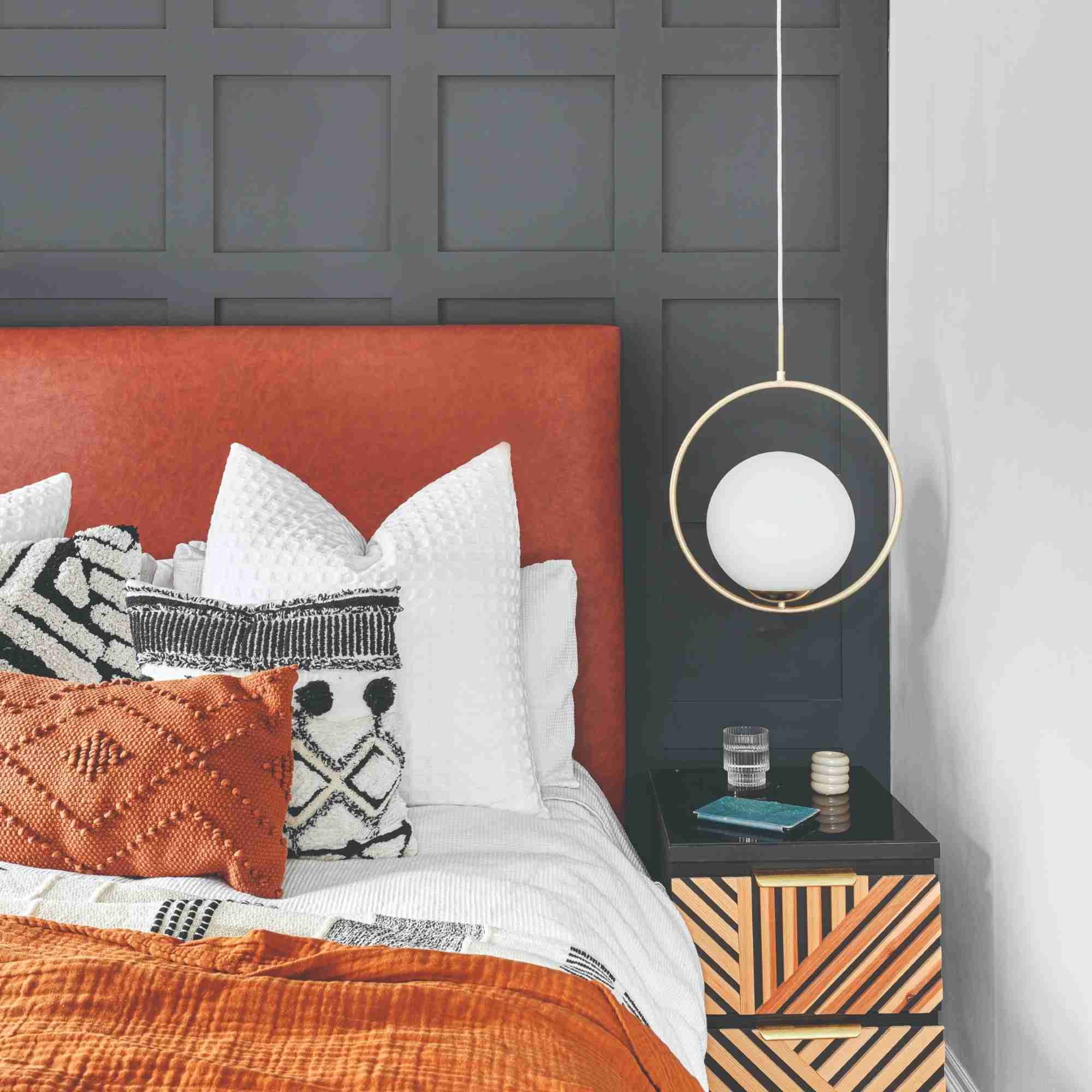 A bedroom with a panelled feature wall painted charcoal with a bed with a rust-coloured leather headboard and terracotta bed linen
