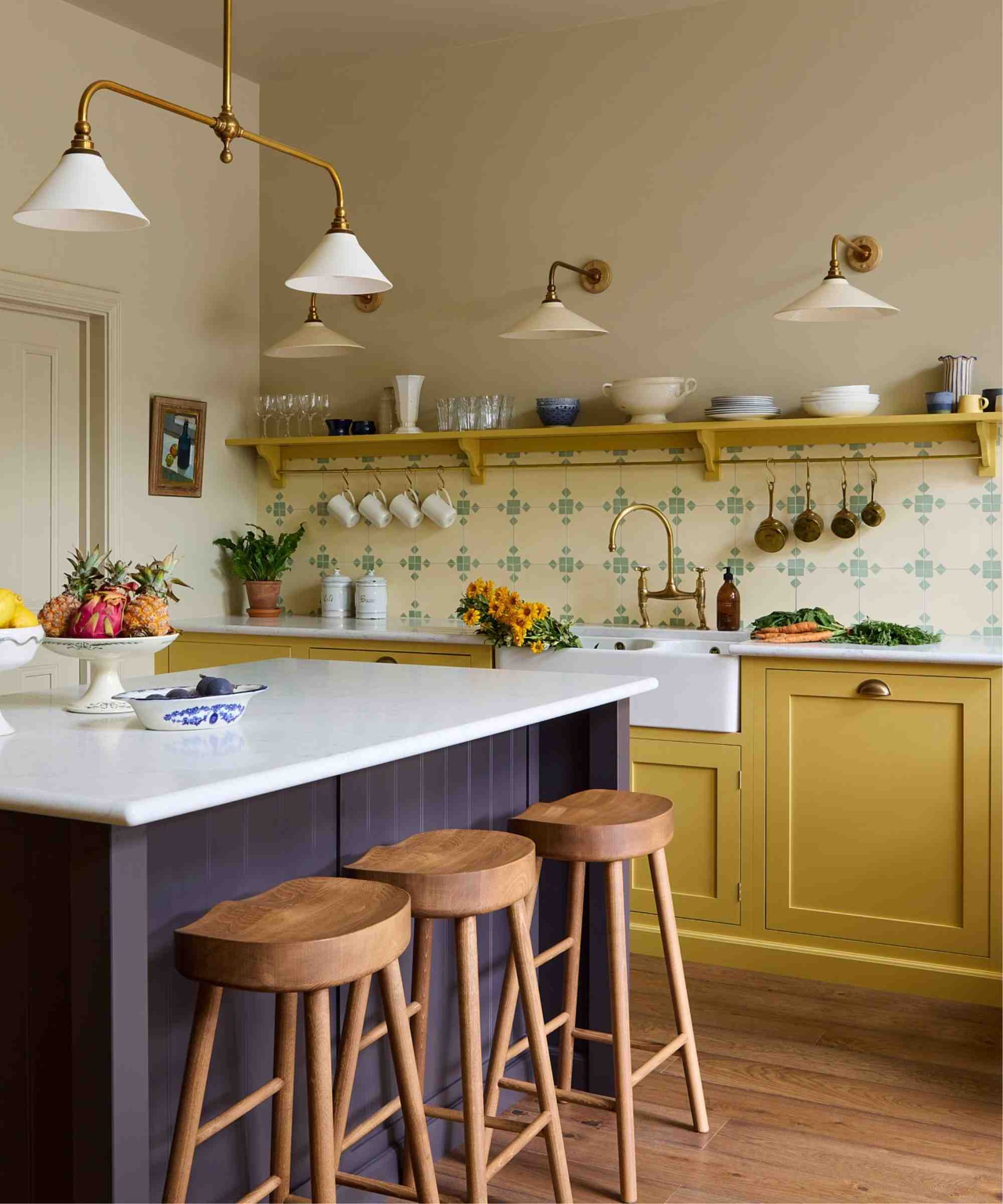 An open plan kitchen with yellow cabinets, and aubergine island, and cream and light green patterned wall tiles